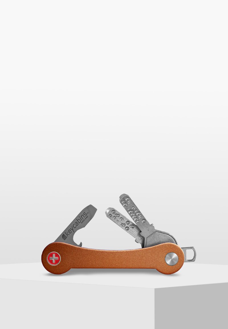 Multiverktyg nyckelhållare med kopparfinish, som har silverfärgade nycklar och ett litet blad, kompakt design med rund ände och logotypdetalj.