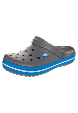 Grå slip-on træsko med ventilationshuller, blå og hvide stribede sål og justerbar hælrem.