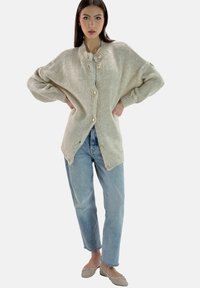 Beige stickad kofta med rund hals, knappförslutning och överdimensionerade ärmar, ihop med ljusblå jeans och platta skor.