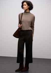 Un pull col roulé beige, un pantalon large noir texturé et des bottines brunes. Un sac à épaule marron complète le look sur un fond neutre.