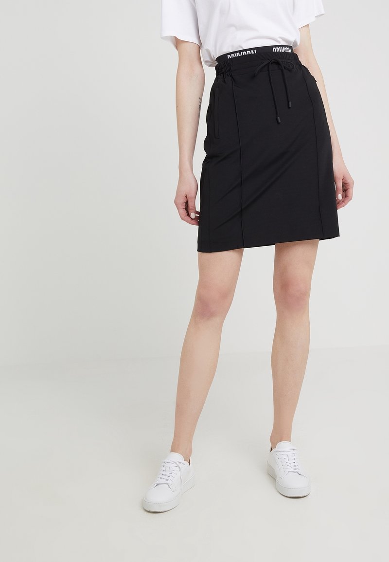 Jupe noire avec une taille élastique dotée d'un cordon de serrage, fabriquée dans un tissu lisse, avec des poches latérales et une coupe à la longueur du genou.