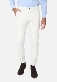 Pantaloni bianchi in cotone con una vestibilità slim, dotati di chiusura a bottone frontale e tasche laterali. Indossati con stivaletti alla caviglia in suede scuro.