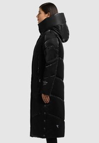 Abrigo acolchado negro con cuello alto, diseño acolchado, bolsillos con cremallera y cierres a presión. Presenta una capucha y textura suave.