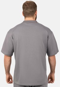 Camicetta grigia a maniche corte in tessuto texturizzato, con scollo rotondo e maniche raglan. Ha una vestibilità ampia e un design minimale.