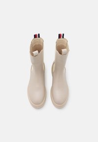 Botas de tobillo beige hechas de cuero suave, con punta redondeada, paneles laterales elásticos y una lengüeta con detalles en rojo, blanco y azul.