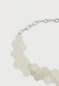 Colier metalic format dintr-o serie de discuri plate, circulare, în nuanță argintie, conectate printr-un lanț reglabil pentru ajustarea lungimii.