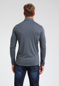 Polo gris de manga larga con cuello con solapa, textura lisa y puños abotonados, combinado con jeans azul oscuro.