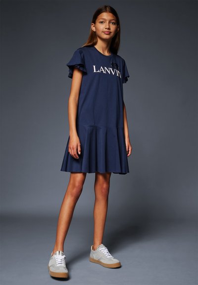 Vestido azul marino de manga corta con un dobladillo acampanado, que presenta el texto blanco "LANVIN". Combinado con zapatillas grises y cordones blancos.