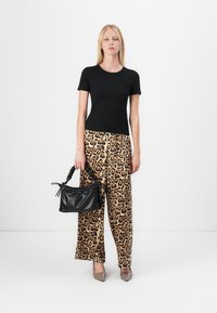 Svart tettsittende t-skjorte, vide bukser med leopardmønster, og svart håndveske med strukturert finish; grå spisse sko fullfører antrekket.