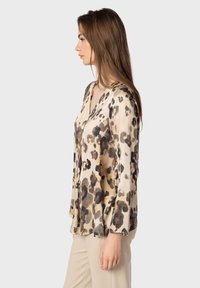 Blusa con stampa leopardata in tessuto leggero, con scollo a V, maniche lunghe e una silhouette fluida, in tonalità di beige e marrone.