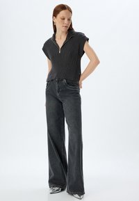 Grå ribbet striktrøje med en lynlåset krave, parret med vide, mørkegrå jeans. Sættet har et afslappet design og en løs pasform.