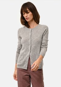 Šedý kardigan z měkké tkaniny, s kulatým výstřihem, dlouhými rukávy, zapínáním na knoflíky a dvěma předními kapsami.