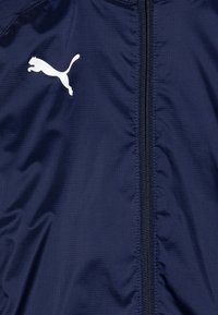 Veste légère bleu marine avec fermeture éclair à l'avant, arborant un logo Puma blanc et un tissu subtilement texturé.