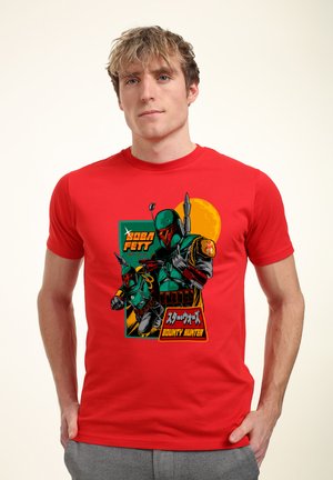 Czerwona koszulka z graficznym motywem postaci w zielonym zbroi, z hełmem i peleryną, oznaczona napisem "Łowca Nagród" w języku japońskim.