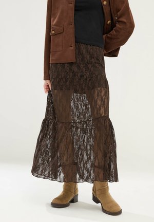 Brązowa koronkowa maxi spódnica noszona z jasnobrązowymi zamszowymi botkami za kostkę i brązową zapinaną na guziki kurtką na czarnym topie.