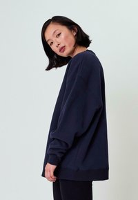 Felpa oversize blu navy con maniche ampie e scollatura a girocollo, realizzata in morbido cotone. Finitura texturizzata e vestibilità comoda.