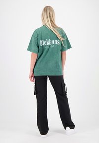 Groen vervaagde katoenen t-shirt met een oversized pasvorm en een logo op de achterkant. Gecombineerd met zwarte cargobroeken met zijzakken en trekkoorden. Witte sneakers.