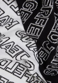 Knitted scarf in black and white features bold, repeated text patterns. Soft texture with contrasting colors highlights graphic design elements.