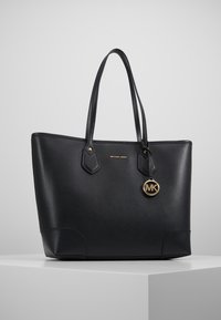 Sac fourre-tout en cuir noir avec une forme structurée, deux poignées, des ferrures dorées et un charm logo. Finition texturée avec des bords angulaires.