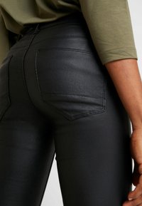 Pantalones de piel sintética negra de tiro alto con una textura suave, que cuentan con dos bolsillos traseros y costuras visibles.