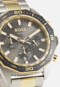 Reloj cronógrafo con pulsera de acero inoxidable y tono dorado, esfera gris oscuro, tres subesferas y bisel tacómetro.
