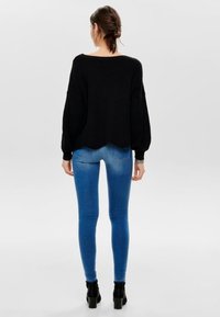 Czarny dziany sweter z szerokimi rękawami, zestawiony z niebieskimi, obcisłymi dżinsami i czarnymi botkami za kostkę. Sweter ma zakrzywiony dół i fakturowany materiał.