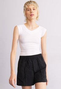 Haut blanc ajusté à manches courtes, associé à un short noir avec taille élastique, doté de poches latérales et d'un tissu texturé.