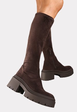 Bottines en suédine marron, montantes jusqu'au genou, avec une semelle épaisse, dotées d'une fermeture éclair sur le côté et d'une finition texturée.