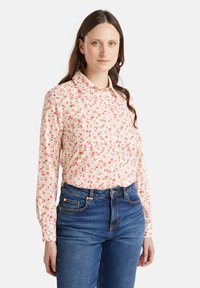 Blusa a maniche lunghe in morbido tessuto rosa chiaro con motivo floreale in rosso e giallo. Presenta un colletto con bottoni e una vestibilità regolare.