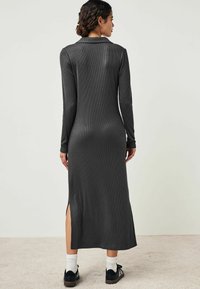 Robe à manches longues côtelée gris foncé, avec des fentes latérales, un col et une coupe ajustée, associée à des chaussures noires et des chaussettes blanches.