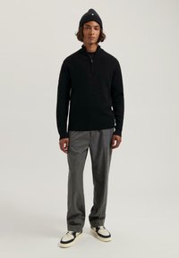 Pulover negru tricotat cu colier cu jumătate de fermoar, asortat cu pantaloni gri plisați și adidași negri și albi. Design simplu cu textură netedă.