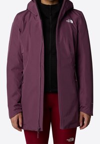 Veste violette résistante aux intempéries avec capuche, fermeture éclair à l'avant, poignets élastiques et détail de logo sur la poitrine, superposée à un haut noir.