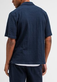 Korte mouwen navy blauwe gestructureerde shirt met een standaard kraag, subtiel patroon en zijsplitten. Draag het met bijpassende navy broek.
