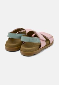 Vaaleanpunaiset ja vihreät sandaalit ristikkäisillä strapsilla; pehmeä nahkainen päällinen, pehmustettu pohja ja kumipohja pitoa varten. Yksinkertainen, toiminnallinen muotoilu.