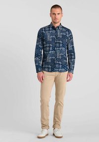 Marineblauwe overhemden met witte geometrische patronen, gecombineerd met lichtbeige broek en witte sneakers. Het overhemd heeft een klassieke kraag en lange mouwen.