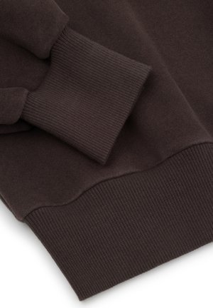 Zbliżenie ciemnobrązowej bluzy z prążkowanymi mankietami i dolnym brzegiem na miękkiej tkaninie.