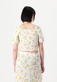 Blommig kort topp med puffärmar i vitt, med gula och gröna mönster. Fyrkantig halsringning och ribbad textur, tillsammans med matchande kjol.