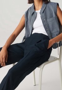 Pantalons larges bleu marine associés à une chemise col ouverte à manches courtes à rayures bleu et blanc. Tissu lisse, coupe décontractée, design minimal.