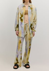 Twee-delig outfit bestaande uit een losse, knoopsluiting shirt en bijpassende broek in een geverfd patroon van groen, paars en geel, gemaakt van gladde stof.