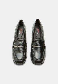 Mocassins en cuir noir au fini lisse, dotés d'une boucle argentée brillante et de semelles intérieures en mousse noire rembourrées. Design classique à bout rond.