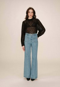 Zwarte kanten blouse met lange mouwen en een ronde hals, gecombineerd met hoog-geprijsde lichtblauwe flared denim broeken. Zwarte puntige schoenen.