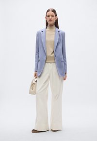 Φωτεινό μωβ σακάκι πάνω από ένα μπεζ ζιβάγκο, σε συνδυασμό με λευκό παντελόνι με φαρδύ πόδι. Συνοδεύεται από μια μικρή κρεμ τσάντα χειρός και καφέ παπούτσια.