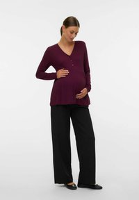 Haut de maternité en tissu côtelé violet profond avec un col en V, des manches longues et des accents de boutons, associé à un pantalon noir ample.
