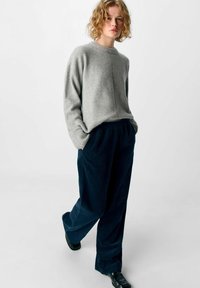 Pull en maille grise avec un col rond et des épaules tombantes, associé à un pantalon large en velours côtelé bleu marine. Texture lisse avec une coupe décontractée.