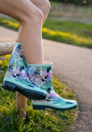 Bottes de pluie en caoutchouc à motifs floraux associant des teintes de vert, bleu, rose et noir. Semelles texturées épaisses, design de hauteur intermédiaire et bords enroulés.