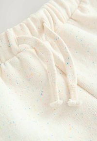 Pantaloni da jogging bianchi con macchie multicolori. Materiale in maglia morbido con vita elastica e cordino per la regolazione.