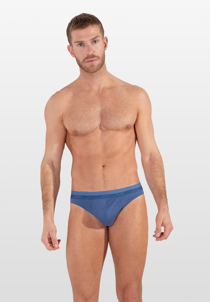 Modré slipy vyrobené z měkké tkaniny s hladkou texturou. Mají opasek s logem. Jednoduchý design, bez vzorů nebo dalších akcentů.