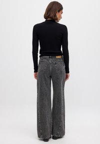 Svart långärmad topp i kombination med högmidjade, vida grå jeans. Jeanserna har en klassisk design med fem fickor och broderade bakfickor.