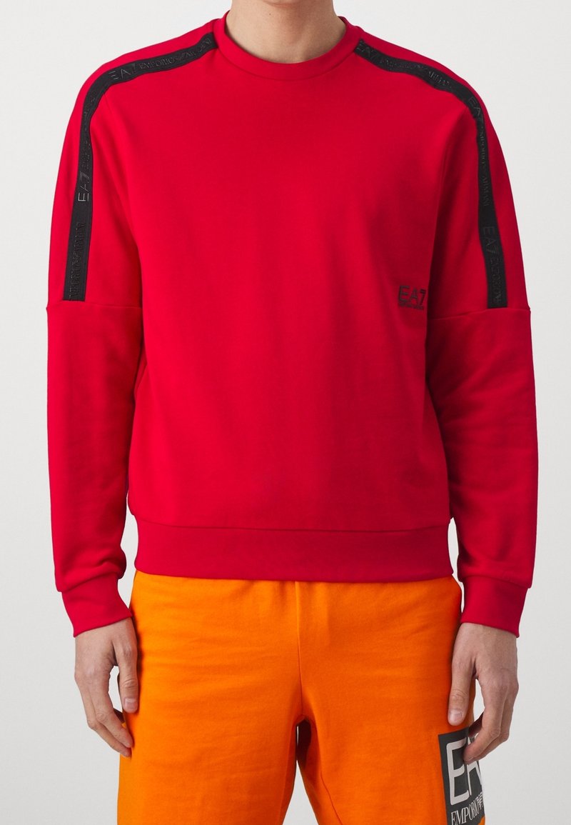 Sudadera roja de tejido suave con acentos negros en los hombros y un detalle de logo. Corte relajado con puños y dobladillo de canalé.