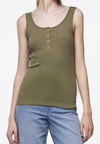 Olivgrön ribbad tanktop med rundad halsringning och fem knappar framtill. Parat med ljusblå jeans.